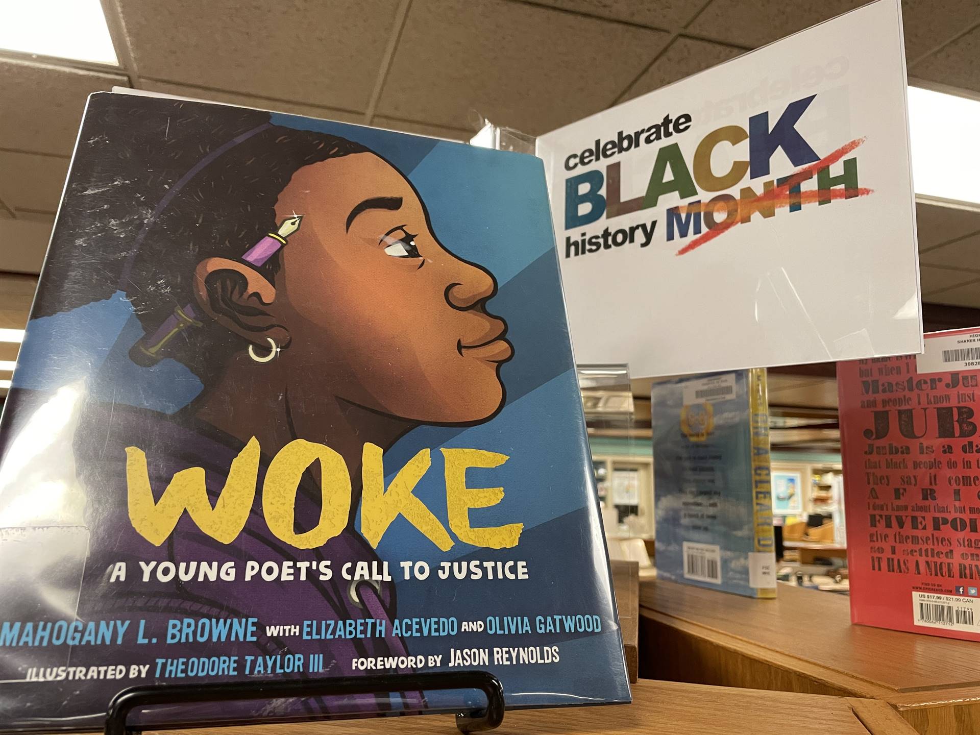 A white sign with the words "celebrate BLACK history" and the word MONTH crossed out and a book titl