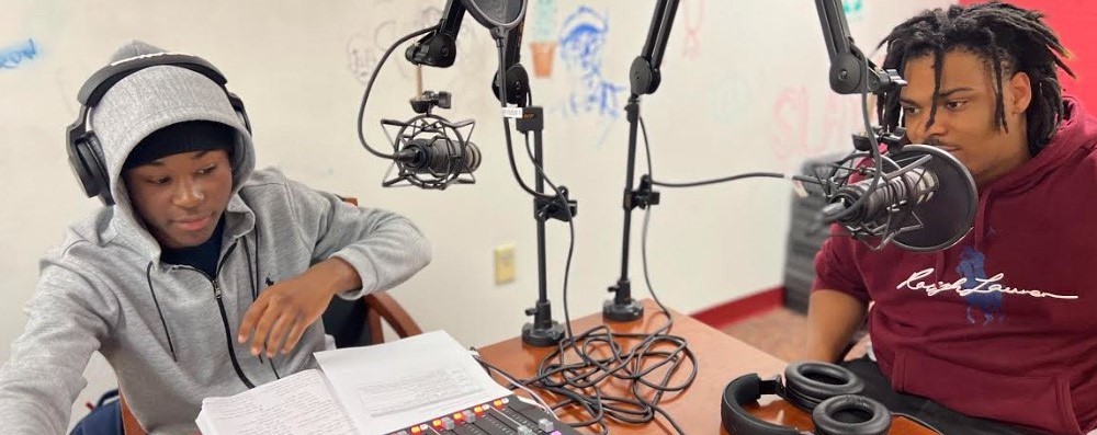 Two students sit at microphones to record a podcast