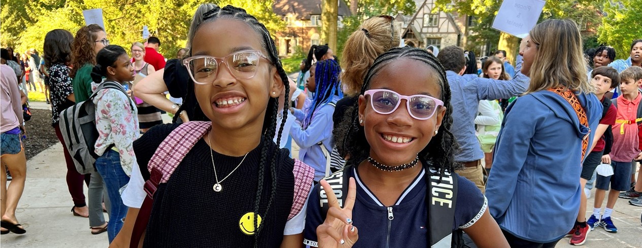 Two smiling female students wearing glasses and one is giving a peace sign